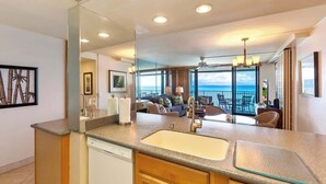 A modern kitchen with a large island, a built-in dishwasher, and a large window overlooking the ocean.