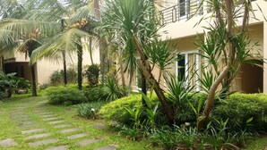 Un patio con un camino empedrado, abundante vegetación y un edificio con balcones.