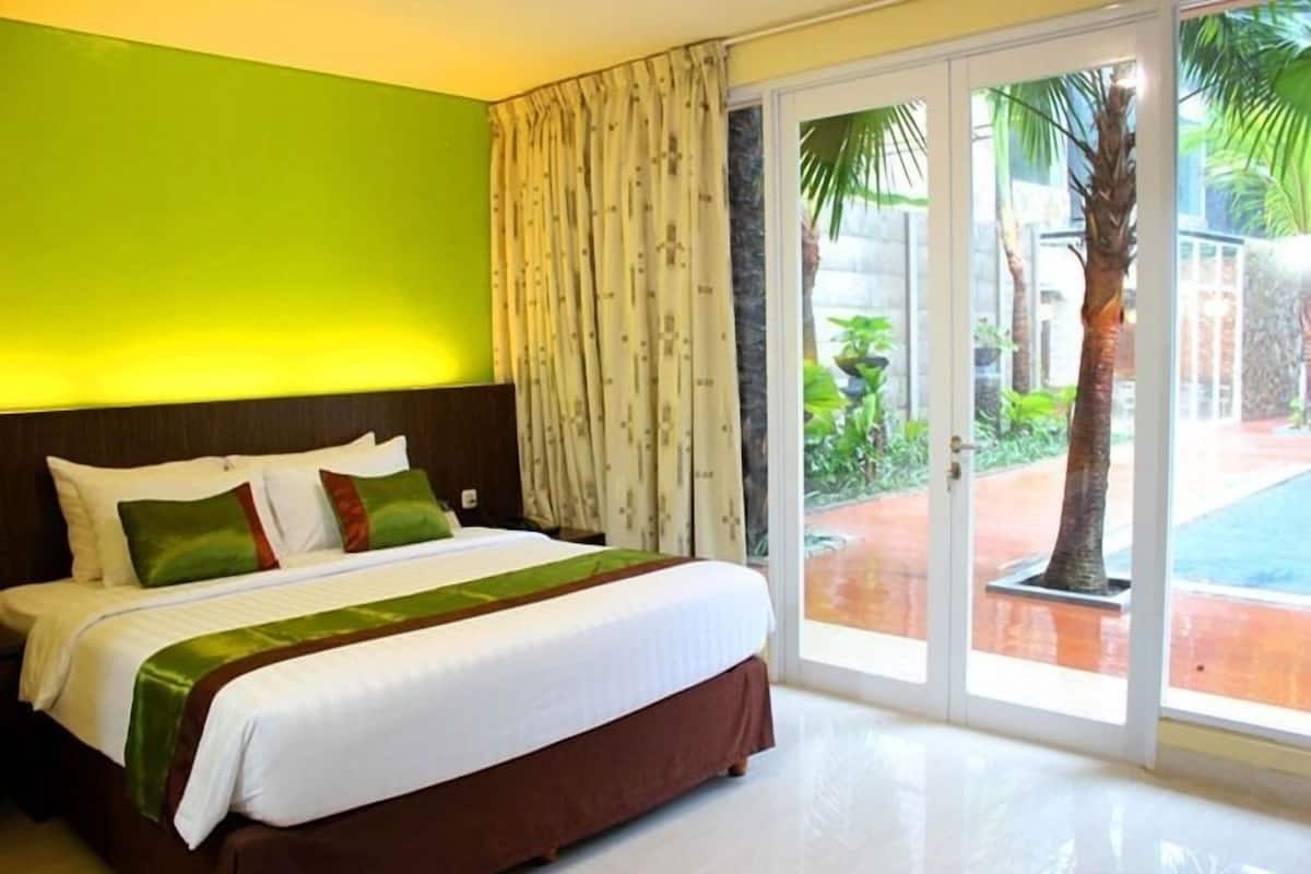 Een hotelkamer met een bed, groene wanden en uitzicht op een zwembad en palmbomen.