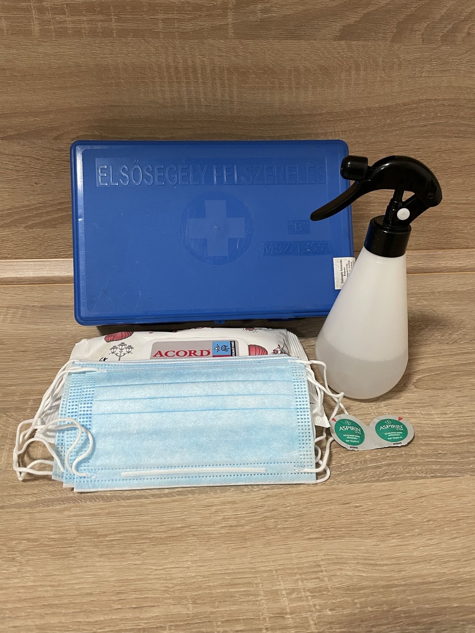 A blue medical kit with a spray bottle, a face mask, and two aspirin packets on a wooden surface.