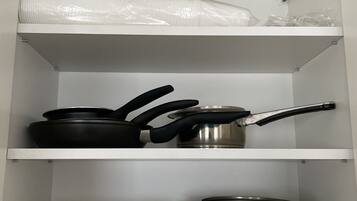 Ett kök med tre kastruller i rostfritt stål på den nedersta hyllan, en stekpanna på den mellersta hyllan och plastpåsar på den översta hyllan.