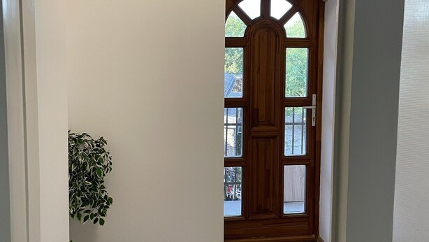 Un pasillo con una puerta de madera, un respiradero en la pared y una planta en maceta.