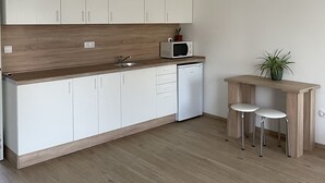 Una cocina moderna con armarios blancos, encimera de madera, microondas, fregadero, lavavajillas y dos taburetes.