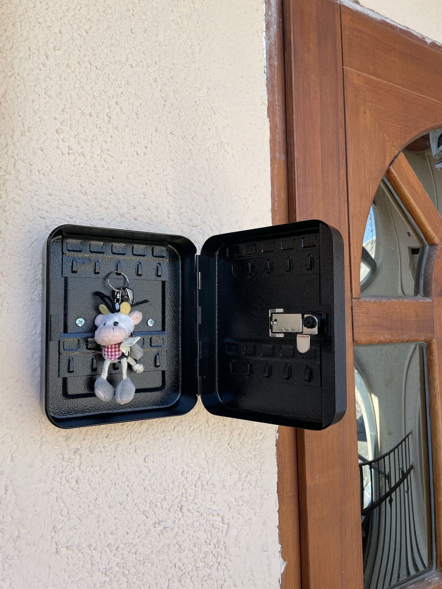 Une boîte noire dotée d’un porte-clés et d’un mécanisme de verrouillage, fixée à un mur texturé à côté d’une porte en bois.