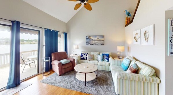 Un salon comprenant un canapé, un fauteuil et une table basse ronde. Un tableau est accroché au mur, et il y a une fenêtre avec des rideaux.