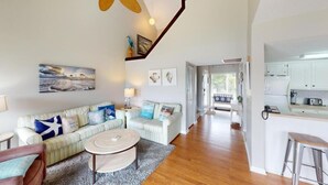 A spacious living room with a sofa, coffee table, and a view into the kitchen. - Heron Marsh Hideaway Split Level Villa (Pawleys Island)