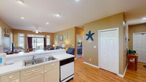 A modern kitchen with a dishwasher, a dining area with a table and chairs, and a living room with a sofa.