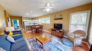 A living room with a sofa, coffee table, and TV, a dining area with chairs, and a kitchen in the background.