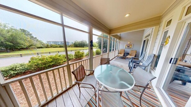 A covered porch with a table and chairs, large windows, and a view of a park and road.