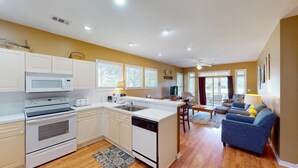 A modern kitchen with white appliances, a dining area with a blue sofa, and a view of the outdoors.