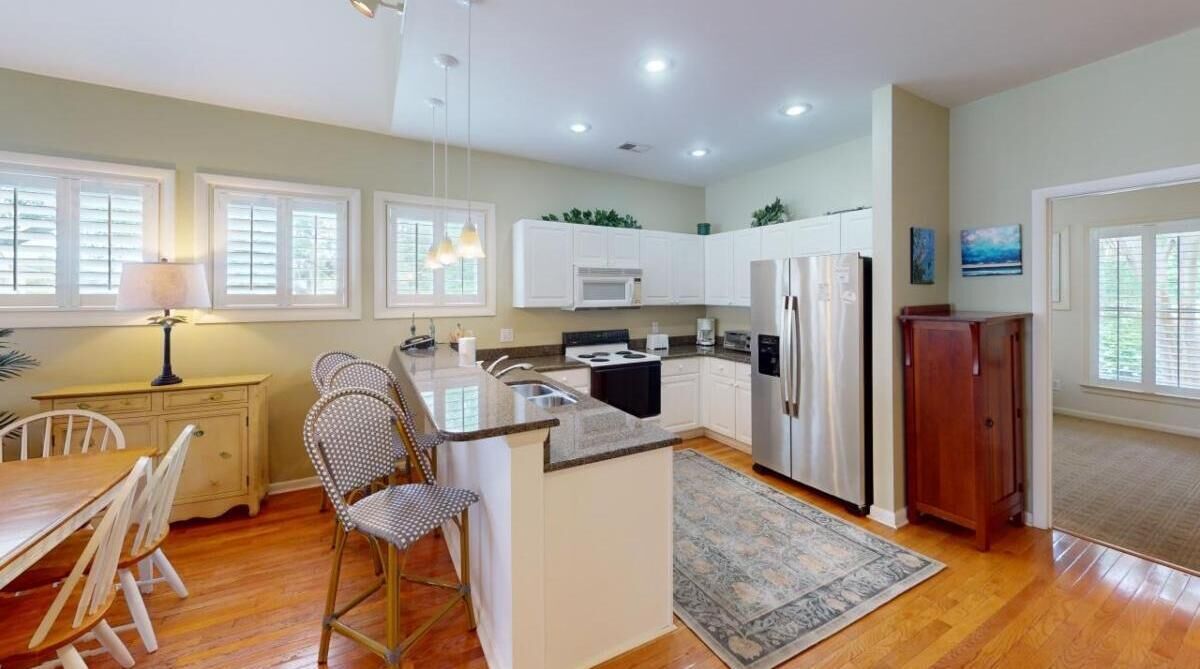 A modern kitchen with white cabinets, a central island, and a dining area with a table and chairs.