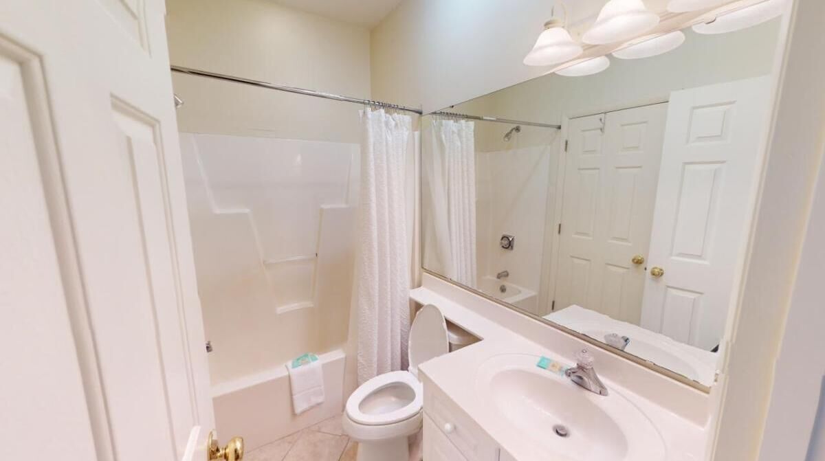 A bathroom with a shower, toilet, sink, and a large mirror.