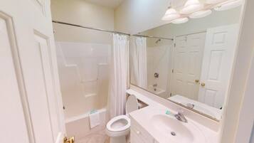 A bathroom with a shower, toilet, sink, and a large mirror.