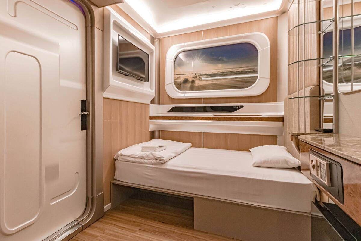 Une pièce compacte et bien éclairée, comprenant un lit, une fenêtre donnant sur un beau paysage, une petite kitchenette et une porte.