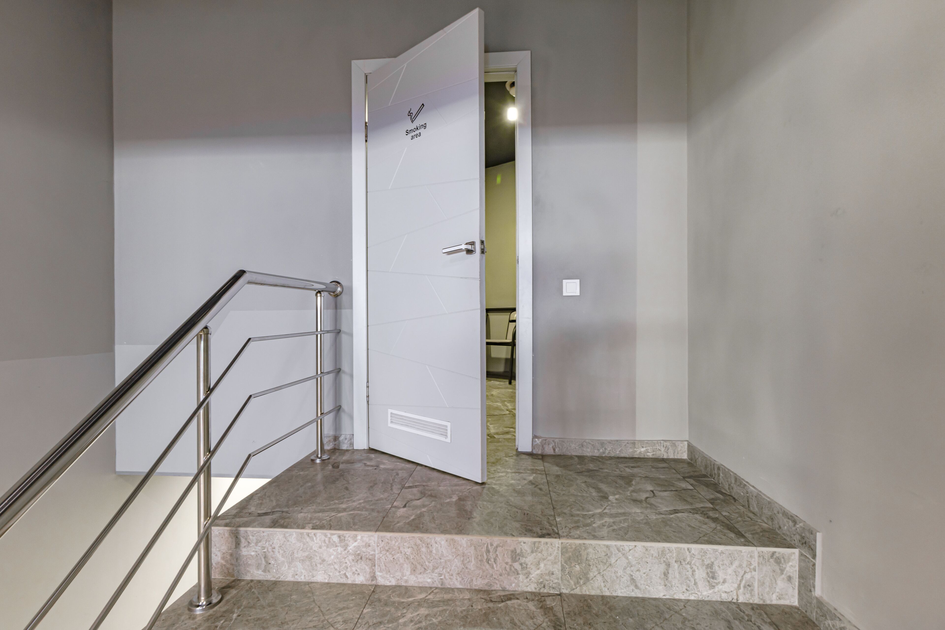 Un escalier avec une rampe métallique menant à une porte indiquant « Zone fumeurs ».