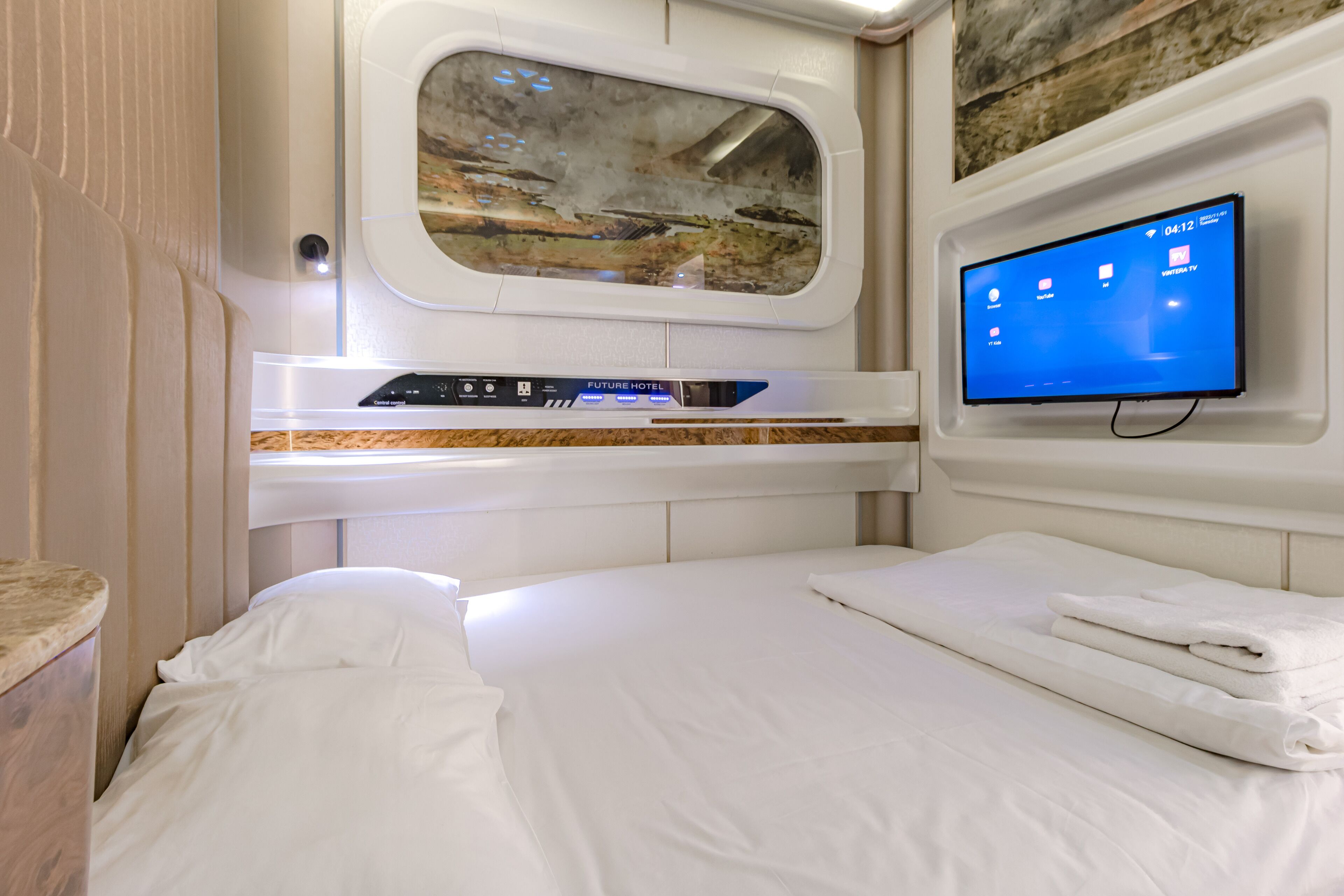 Ein modernes Hotelzimmer mit großem Fenster, Flachbildfernseher, Bedienfeld und ordentlich bezogenen Betten.