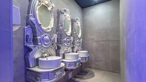 Een rij futuristische, hightech wastafels met verlichte spiegels en een betegelde vloer.