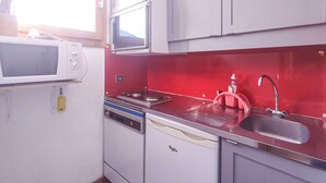 Kompakti keittiö, jossa on mikroaaltouuni, liesi, pesuallas ja punainen välitila.
