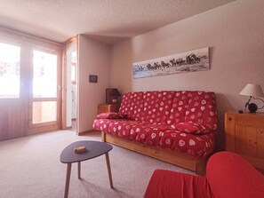 A cozy living room with a red sofa, a small table, and a lamp. - Large divisible studio, ski-in/ski-out in Valmorel, near shops (Valmorel)
