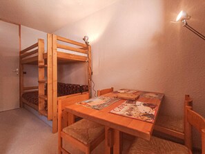 A room with a bunk bed, a wooden table with a placemat, and a lamp.