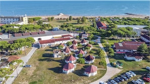 Vista aérea de un pueblo costero con playa, edificios blancos con tejados rojos, y un edificio grande blanco con tejado rojo.