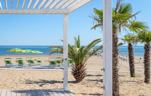 A beach view with a wooden deck, palm trees, and beach chairs under umbrellas. - Beautiful apartment in Cavallino-Treporti with WiFi (Cavallino-Treporti)