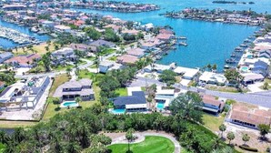 Vue aérienne d’un quartier résidentiel situé sur la côte, avec des maisons, un port de plaisance et une piscine.