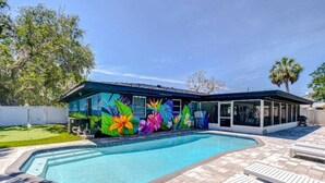 Une piscine agrémentée d’une fresque colorée sur le bâtiment adjacent, et entourée de chaises longues.