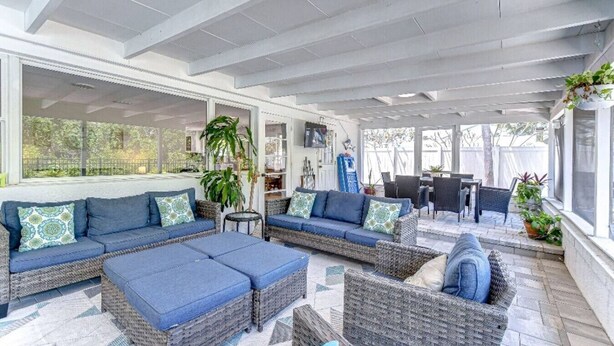 Un patio couvert aménagé avec des meubles en osier, notamment des canapés et une table basse, ainsi qu’une table à manger avec des chaises.