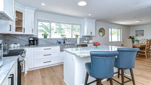 Une cuisine moderne avec des meubles blancs, un plan de travail en marbre et un îlot central doté de tabourets de bar.