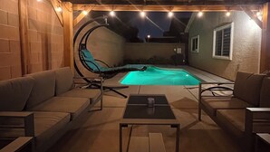 Patio esterno con piscina, posti a sedere e luci decorative.