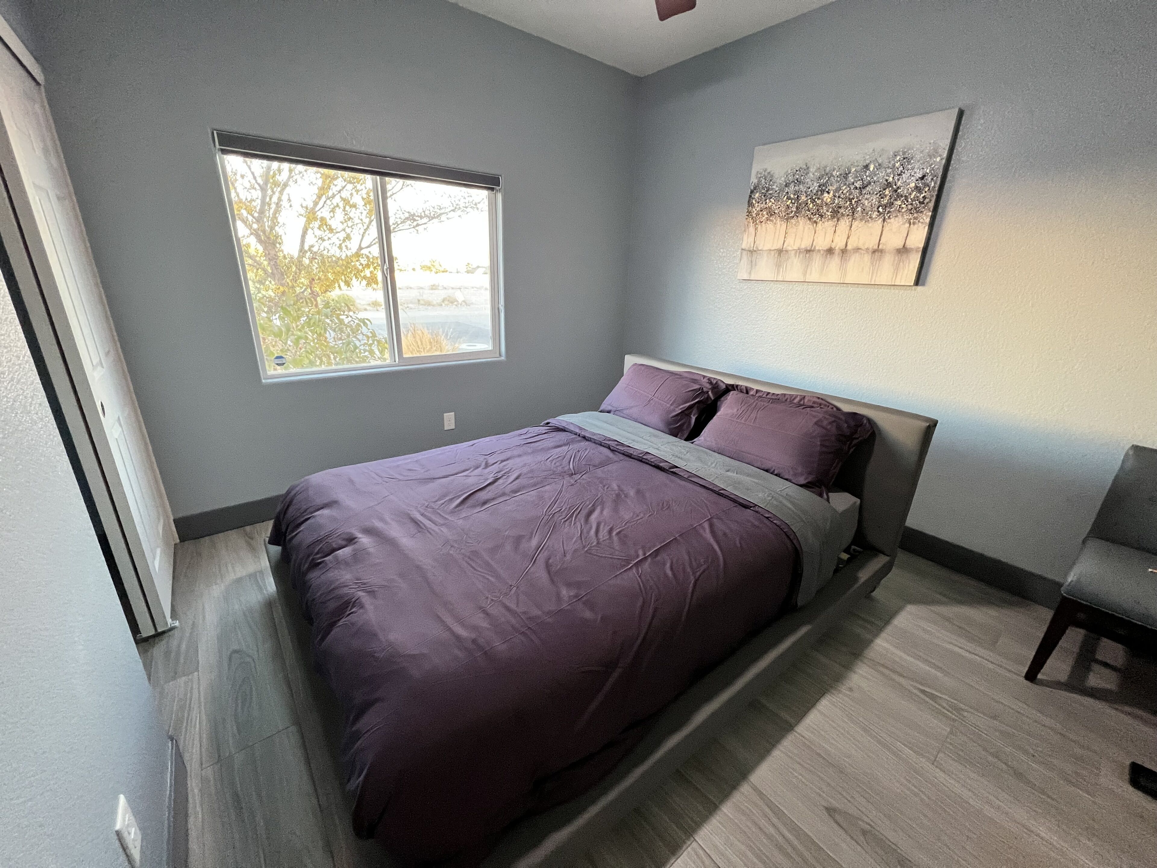 Une chambre à coucher avec un lit, une fenêtre, une chaise et un tableau accroché au mur.