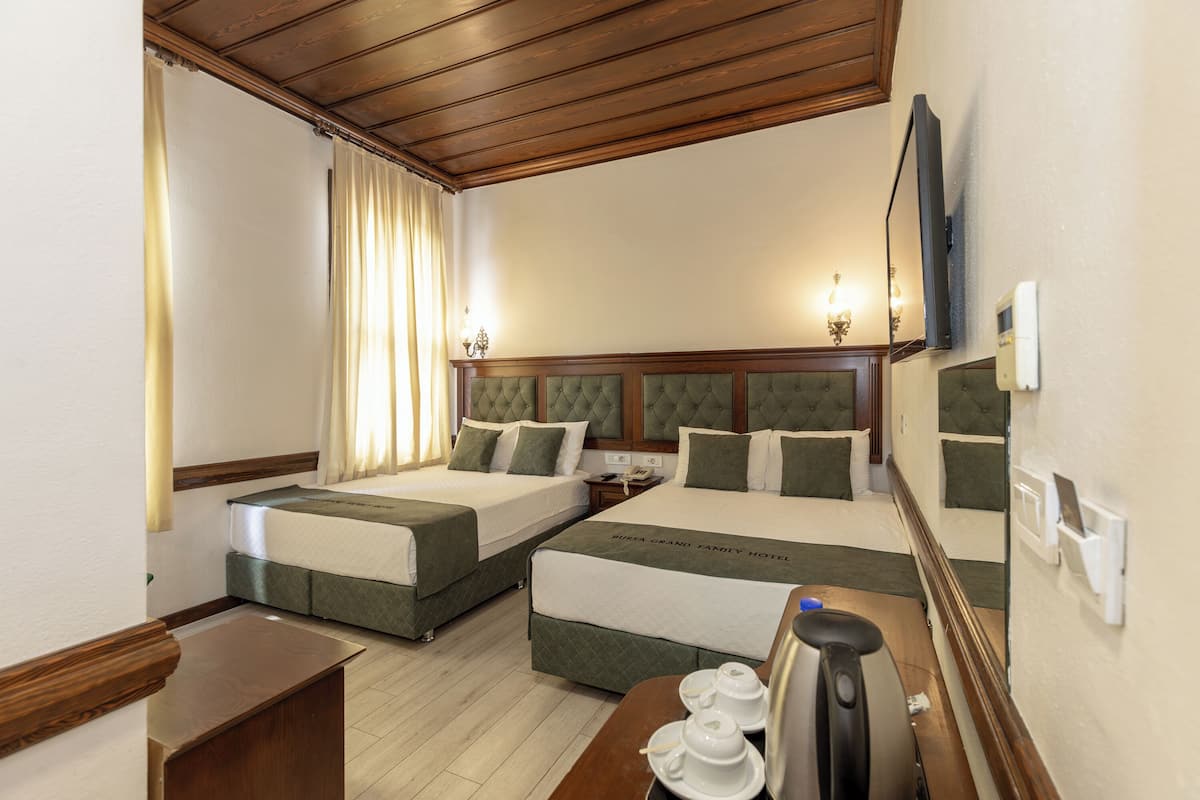 A hotel room with two beds, a wooden ceiling, a flat-screen TV, and a bedside table with a kettle and cups.