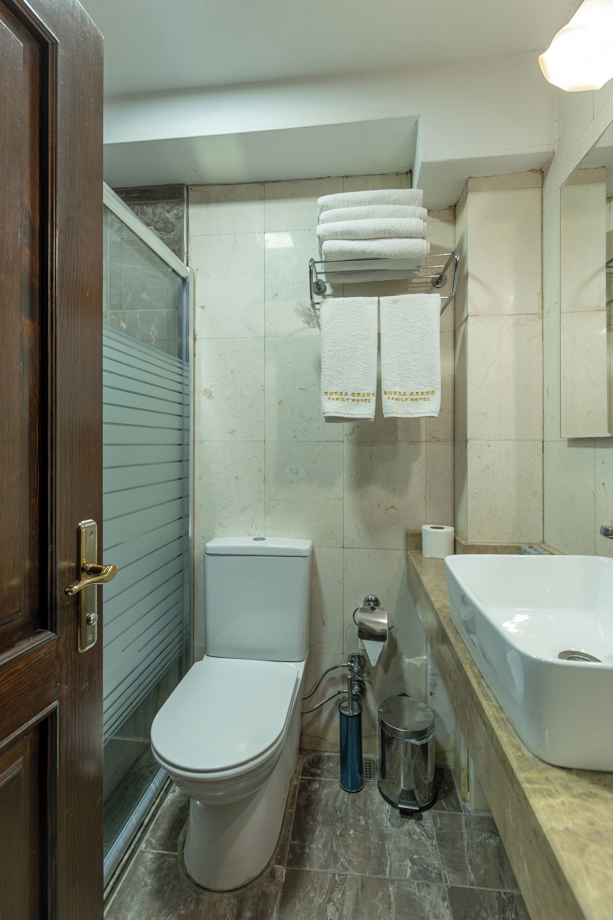 A bathroom with a toilet, a shower, a sink, and a bathtub. There are towels hanging on a rack and a trash can.