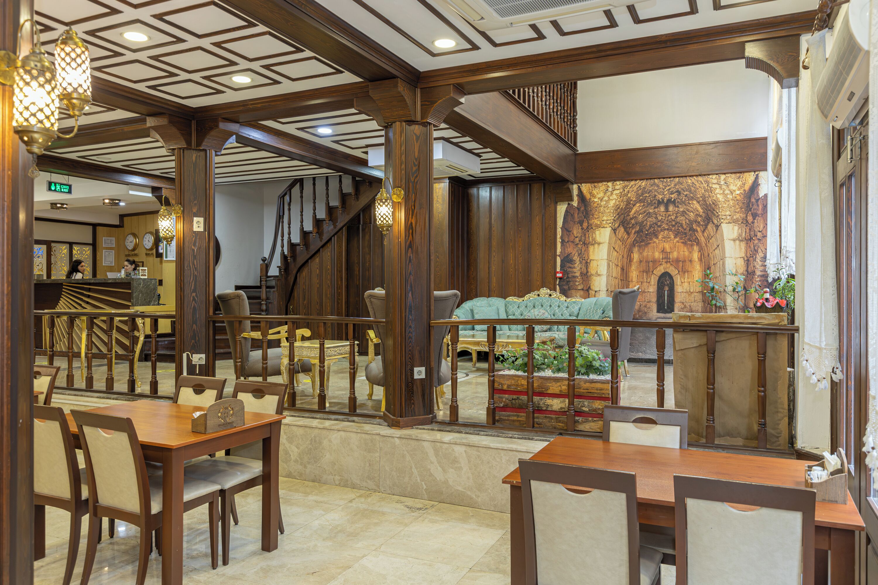 Un hall d’hôtel avec un escalier en bois, un comptoir d’accueil et un espace repas comprenant des tables et des chaises.