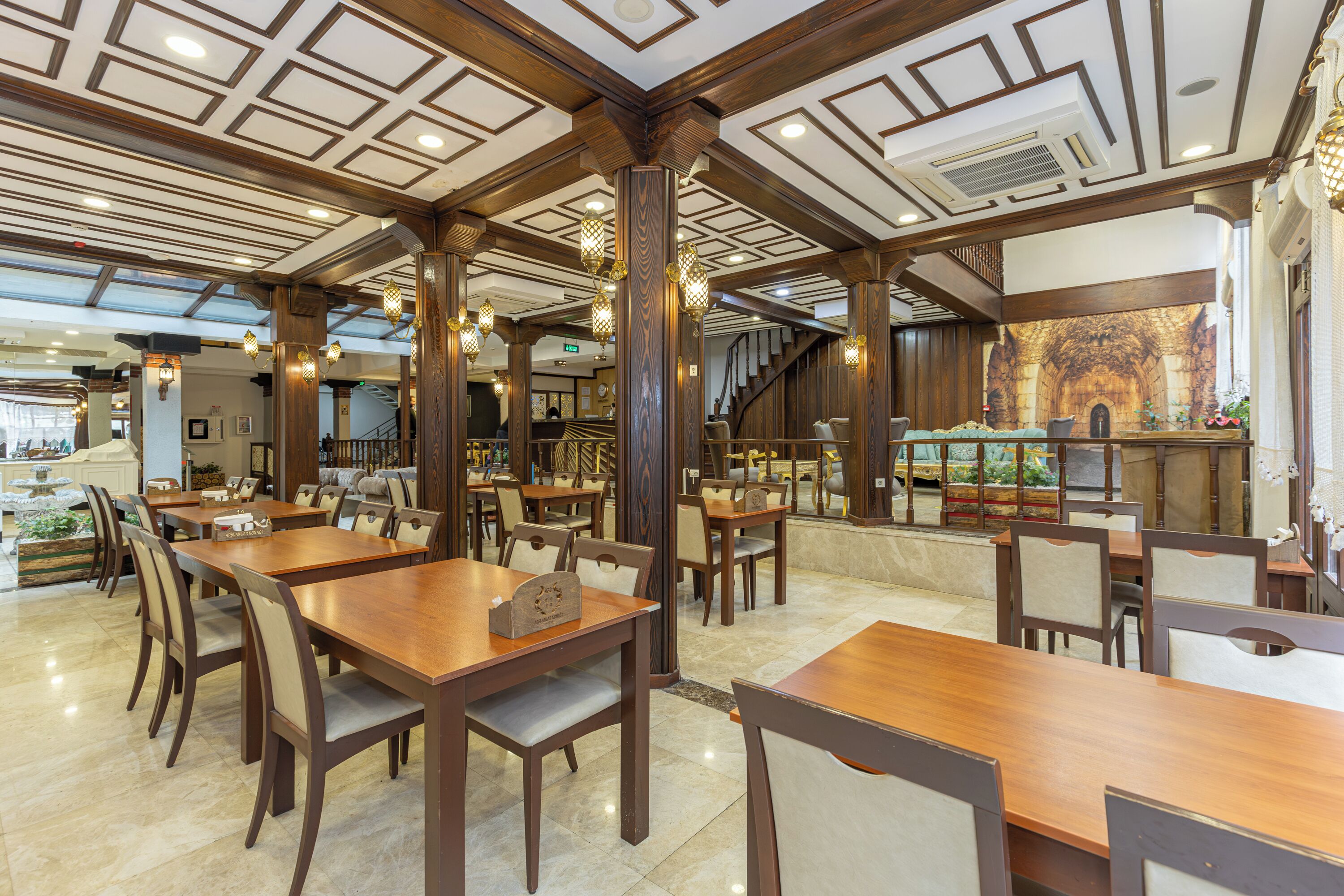 A spacious restaurant with wooden tables and chairs, a high ceiling with intricate designs, and a mural on the back wall.