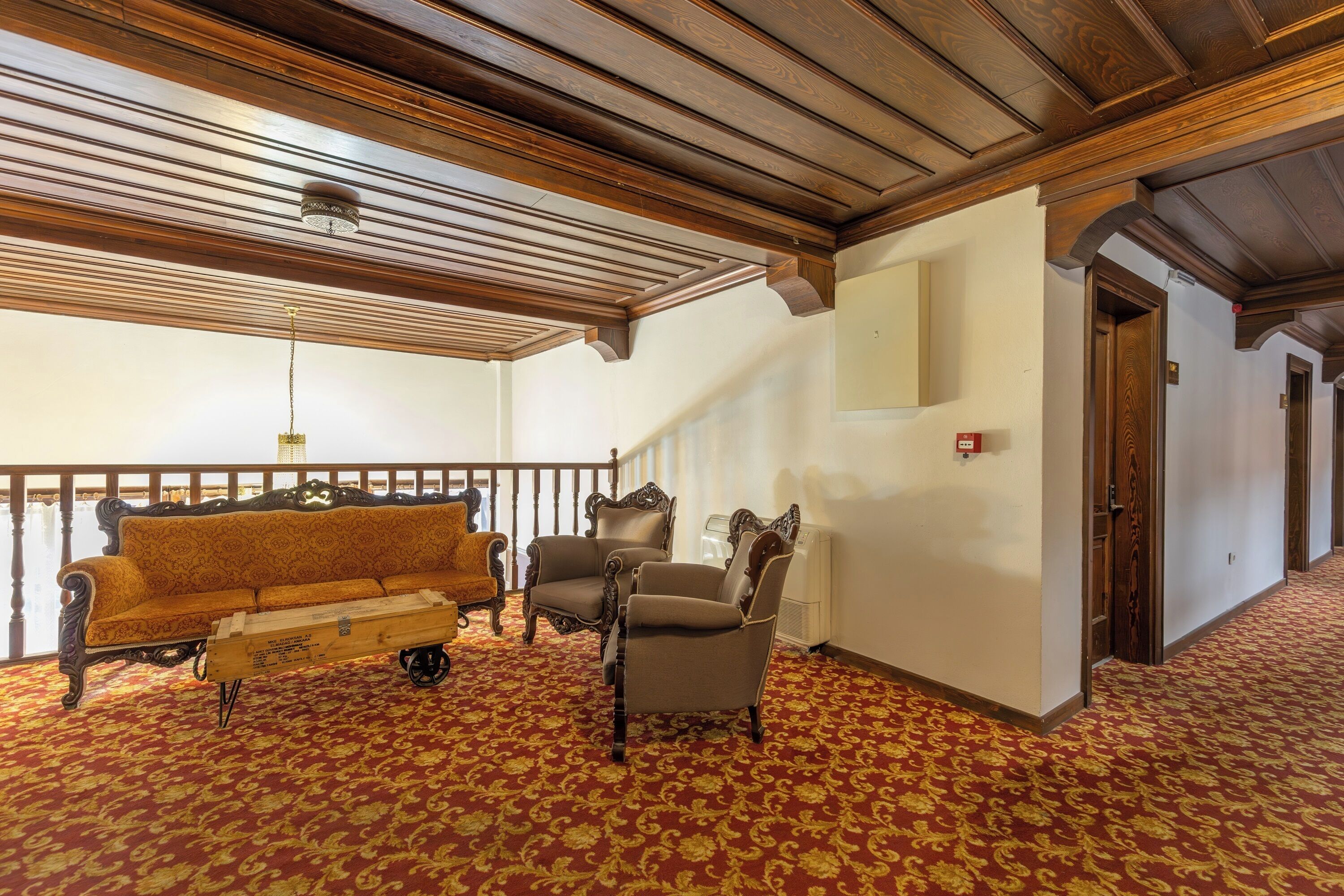 Una habitación con techo de madera, alfombra roja estampada, un sofá, dos sillones y una pequeña mesa.