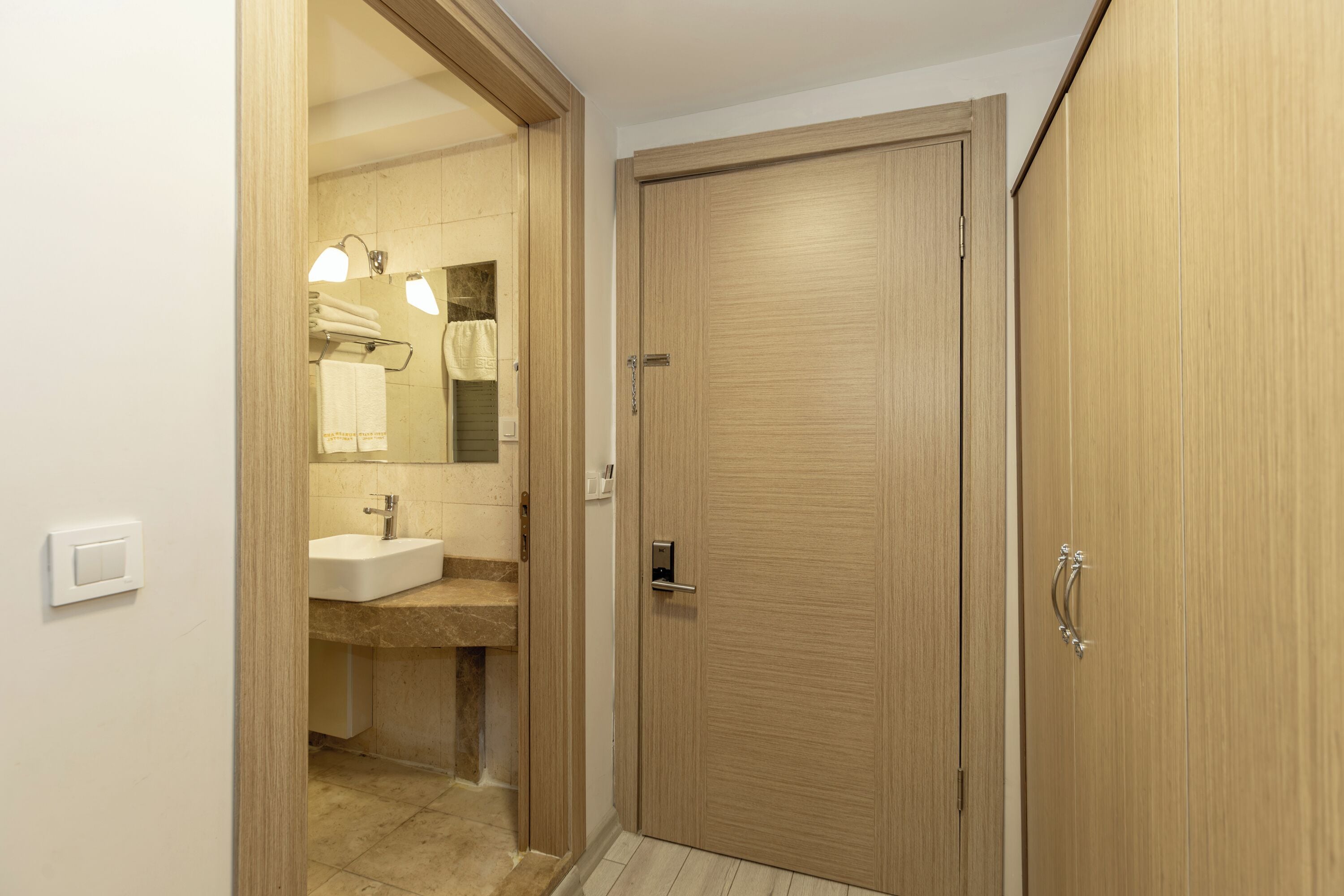 A wooden door with a handle, a bathroom with a sink and mirror, and a towel rack.