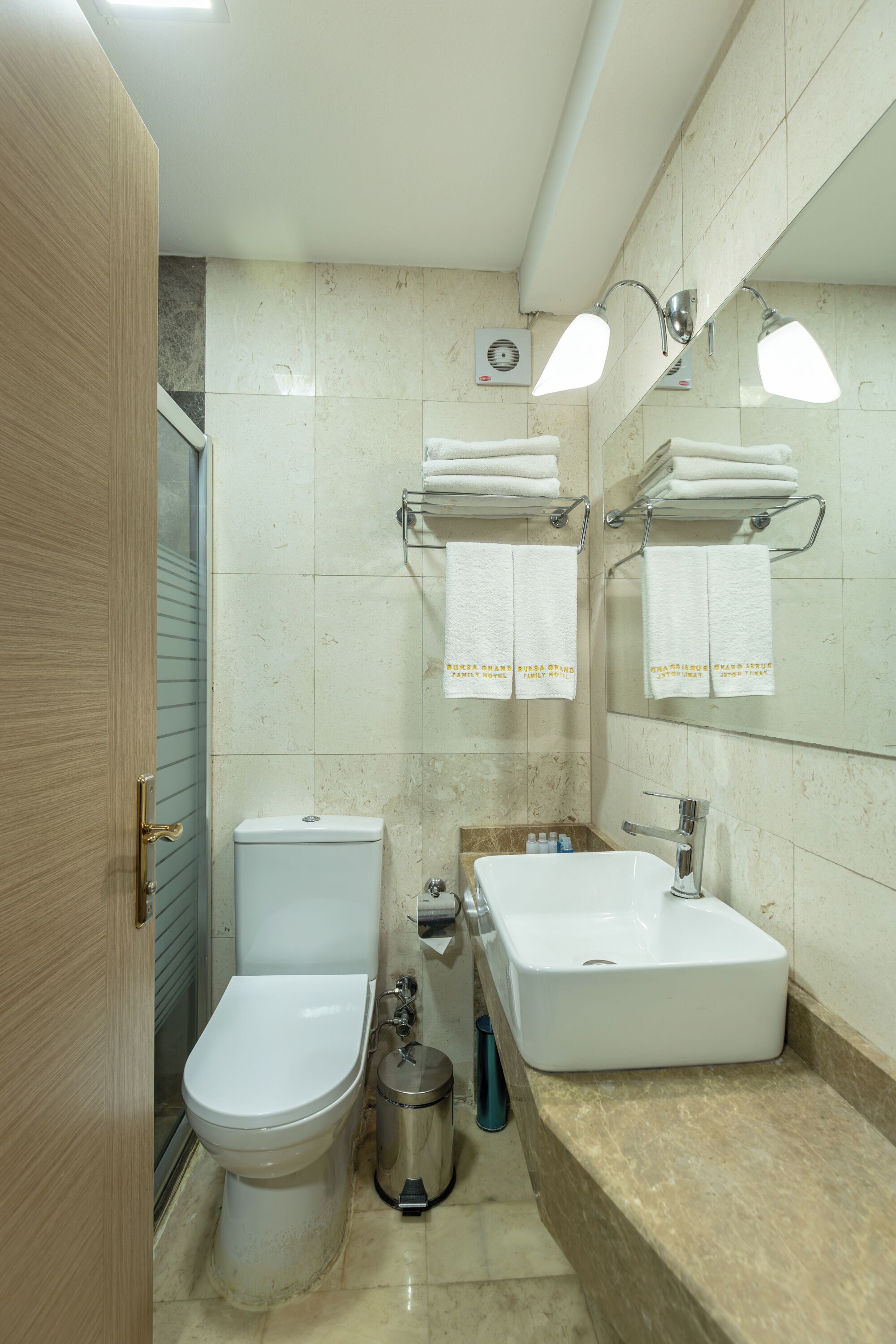 Et badeværelse med toilet, bidet, vask og et spejl med håndklædeholdere.