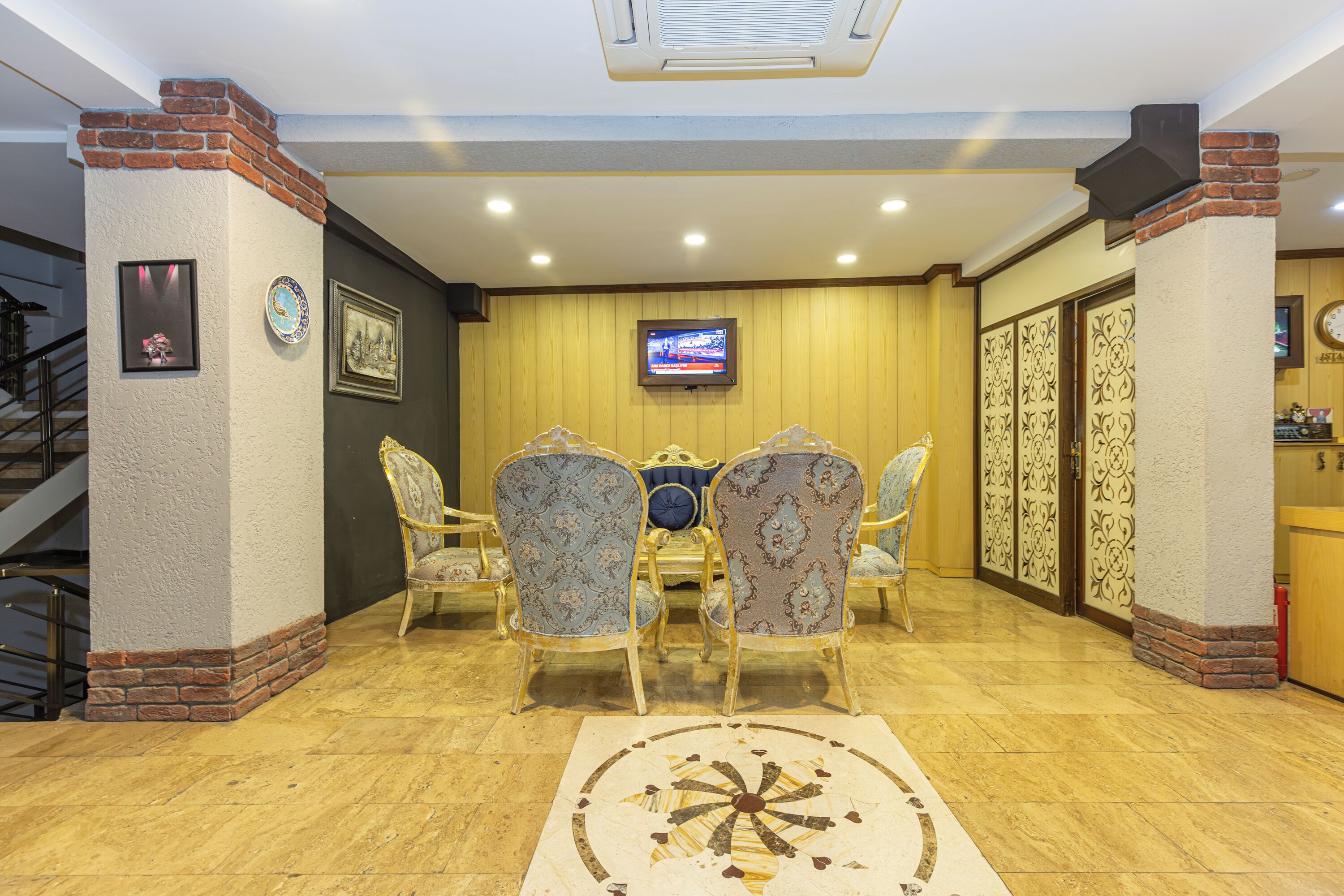 A lobby with a wooden floor, a round table with chairs, a television mounted on the wall, and a staircase to the left.