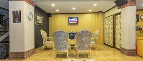 A lobby with a wooden floor, a round table with chairs, a television mounted on the wall, and a staircase to the left.