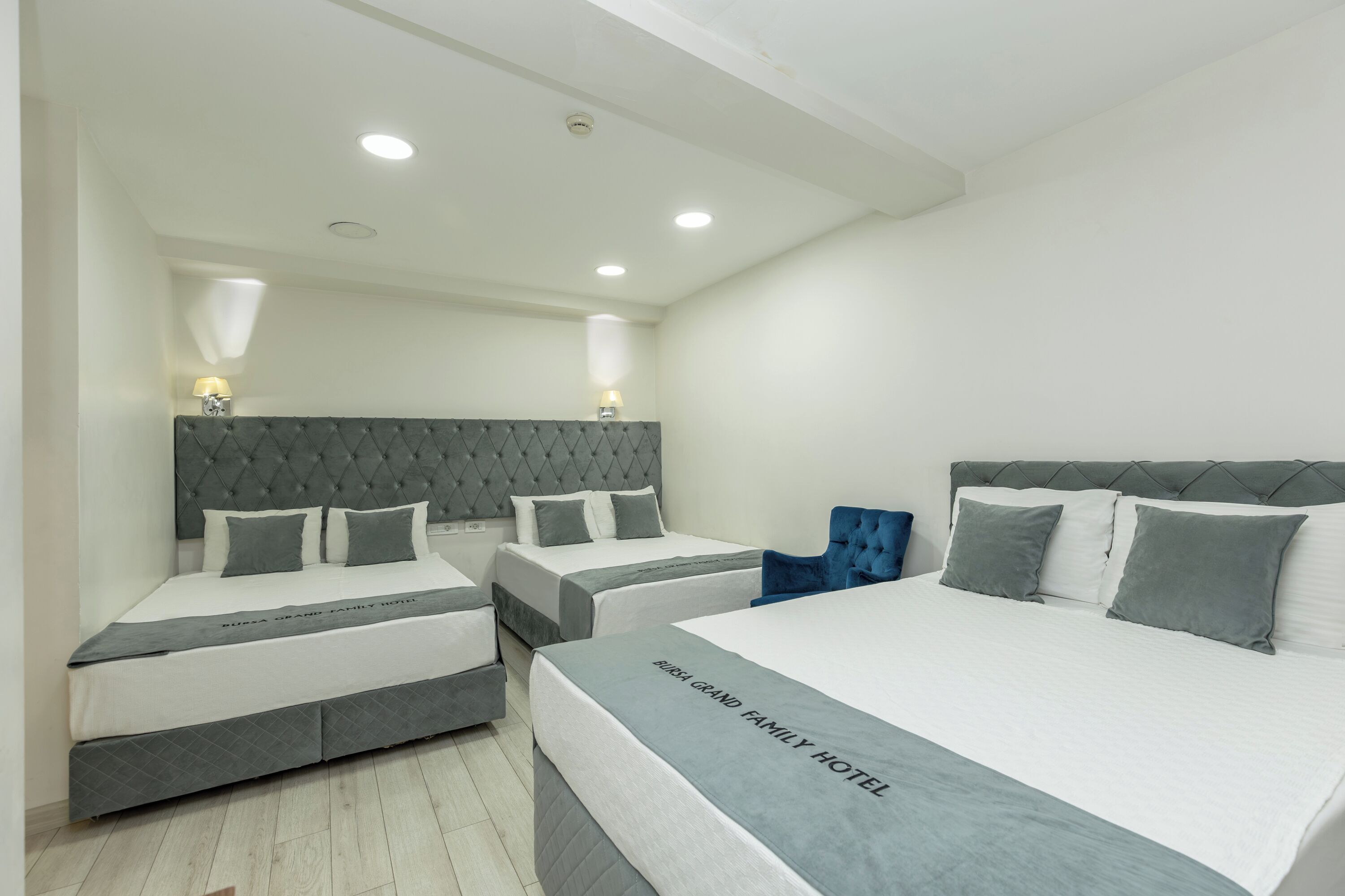Una habitación de hotel con dos camas individuales, una cama grande y una silla azul.