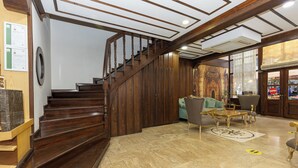A staircase leading to a second floor, a seating area with a sofa and armchairs, and a shop with a visible sign.