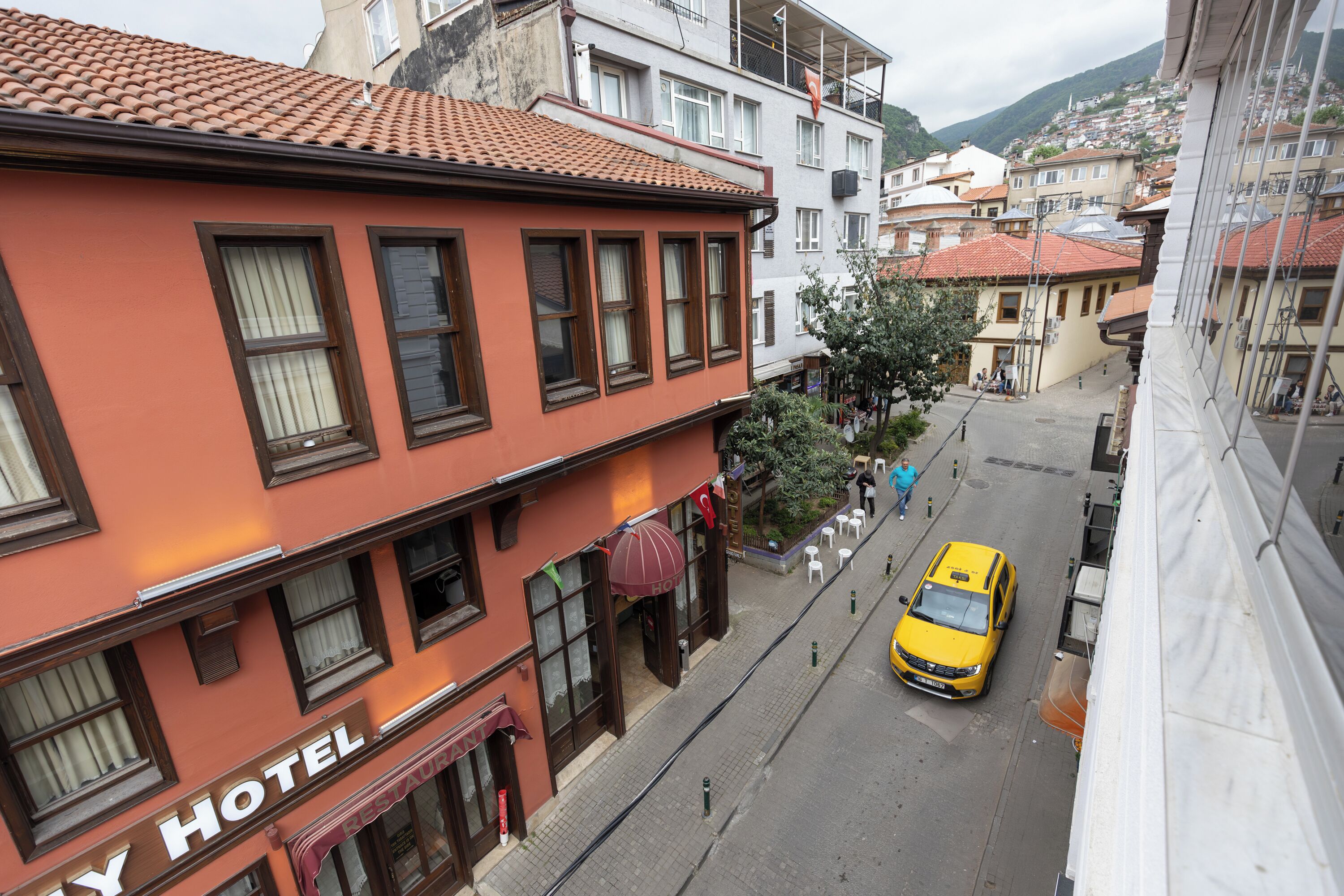 A hotel with a red facade, multiple windows, and a visible street with a yellow taxi.