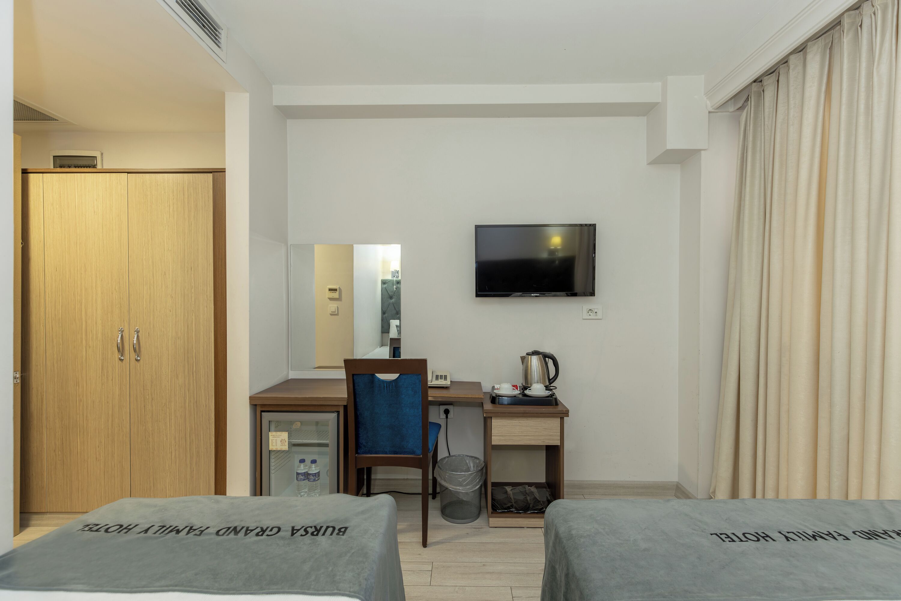 Quarto de hotel com cama, escrivaninha, cadeira, televisão e guarda-roupa.