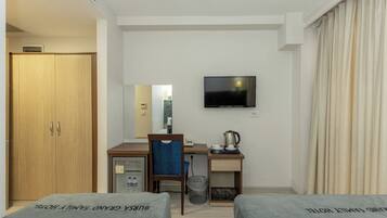 Quarto de hotel com cama, escrivaninha, cadeira, televisão e guarda-roupa.