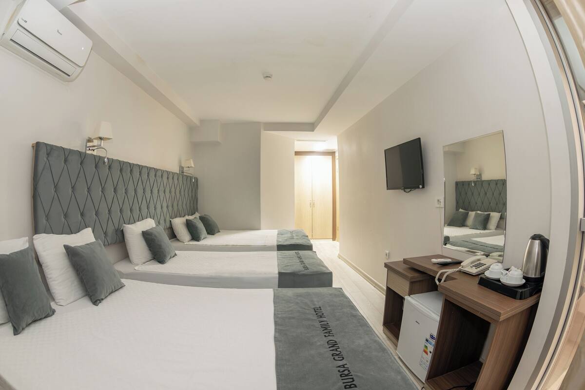 A hotel room with two beds, a desk with a telephone and coffee maker, a small refrigerator, and a television mounted on the wall.