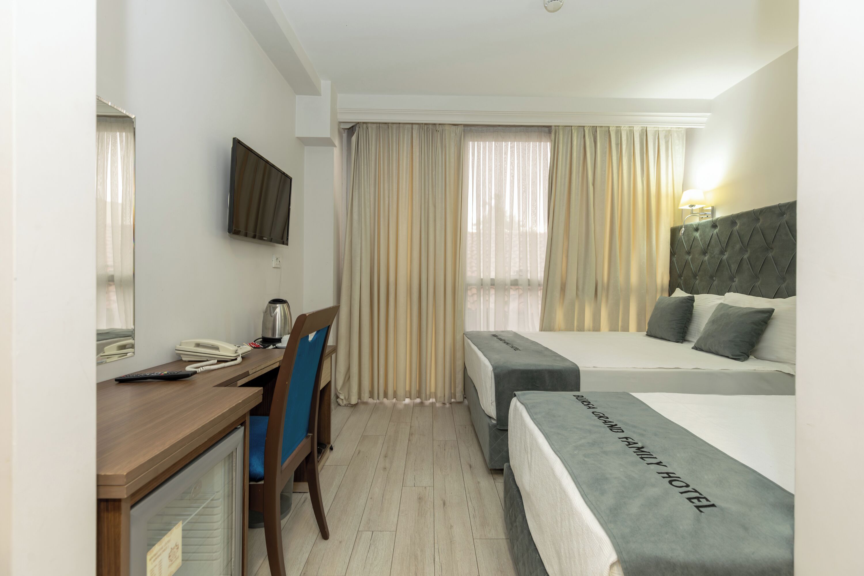 A hotel room with a desk, chair, bed, and a television on the wall.
