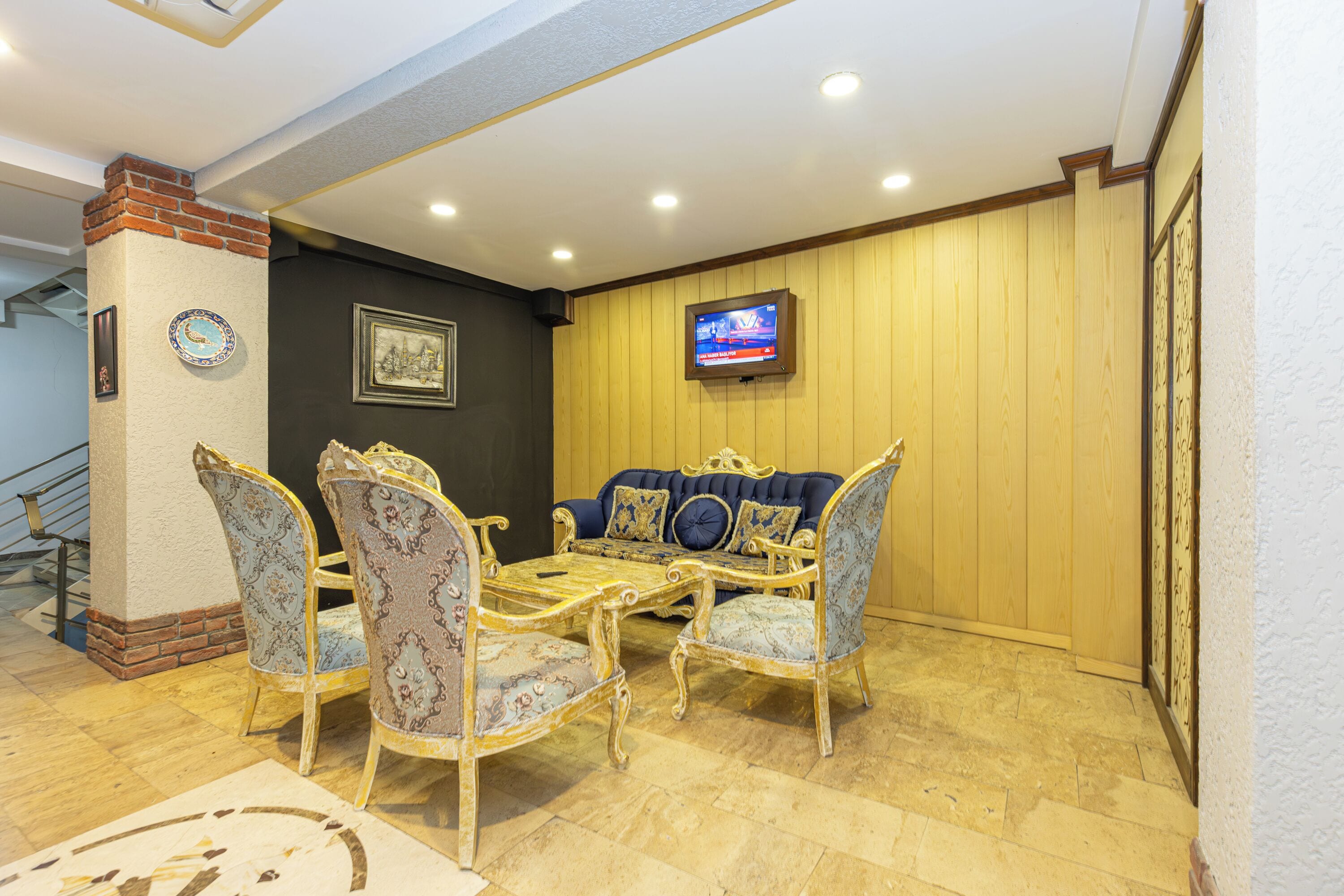 A dining area with a wooden wall, a television mounted above a sofa, and a staircase in the background.