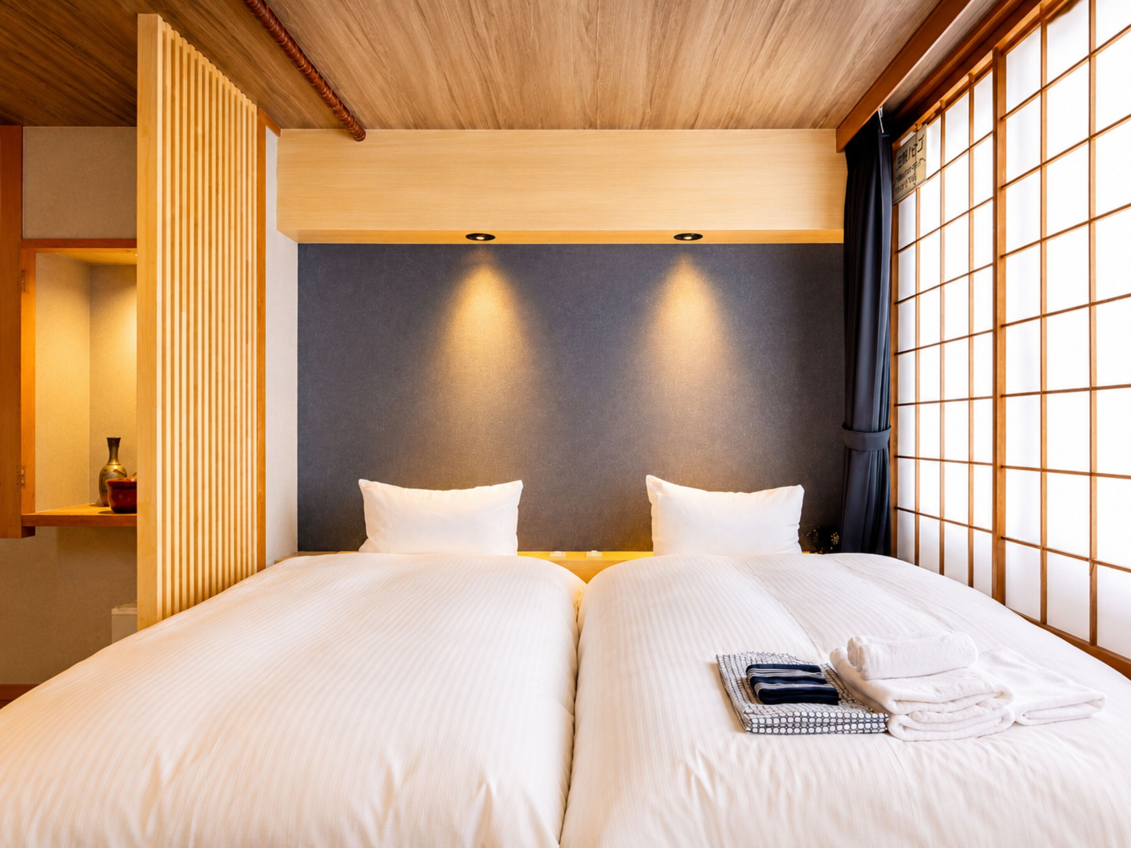 A hotel room with two beds, a wooden ceiling, and a view through a shoji screen.